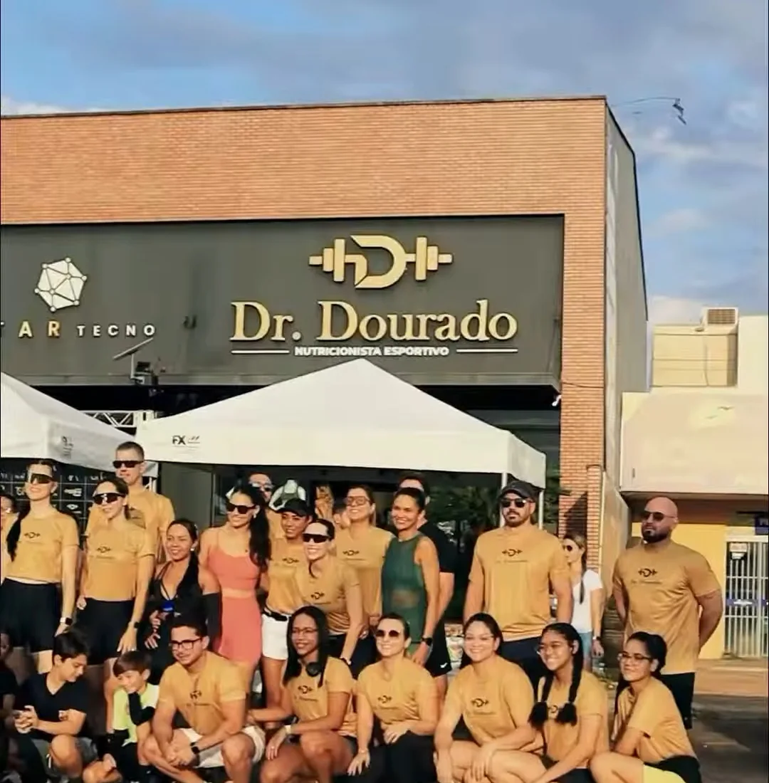 Grupo de participantes com camisetas douradas reunido diante da fachada da clínica Dr. Dourado no dia da corrida