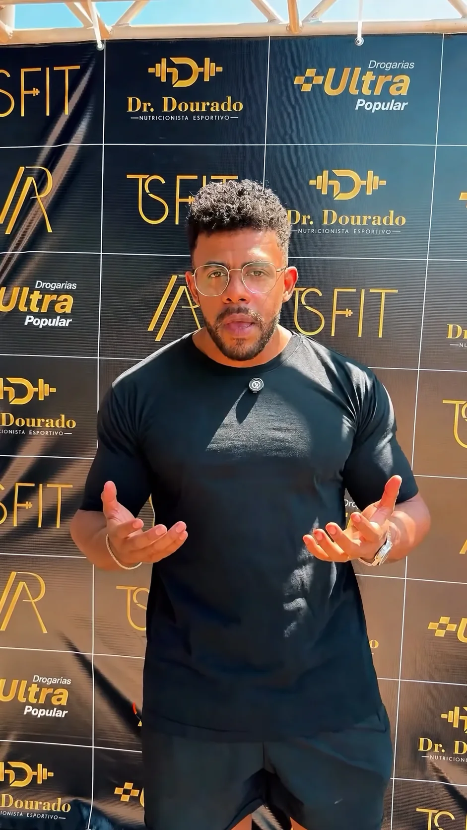 Dr. Dourado diante do painel do evento com as marcas Dr. Dourado, TS Fit e Drogarias Ultra Popular